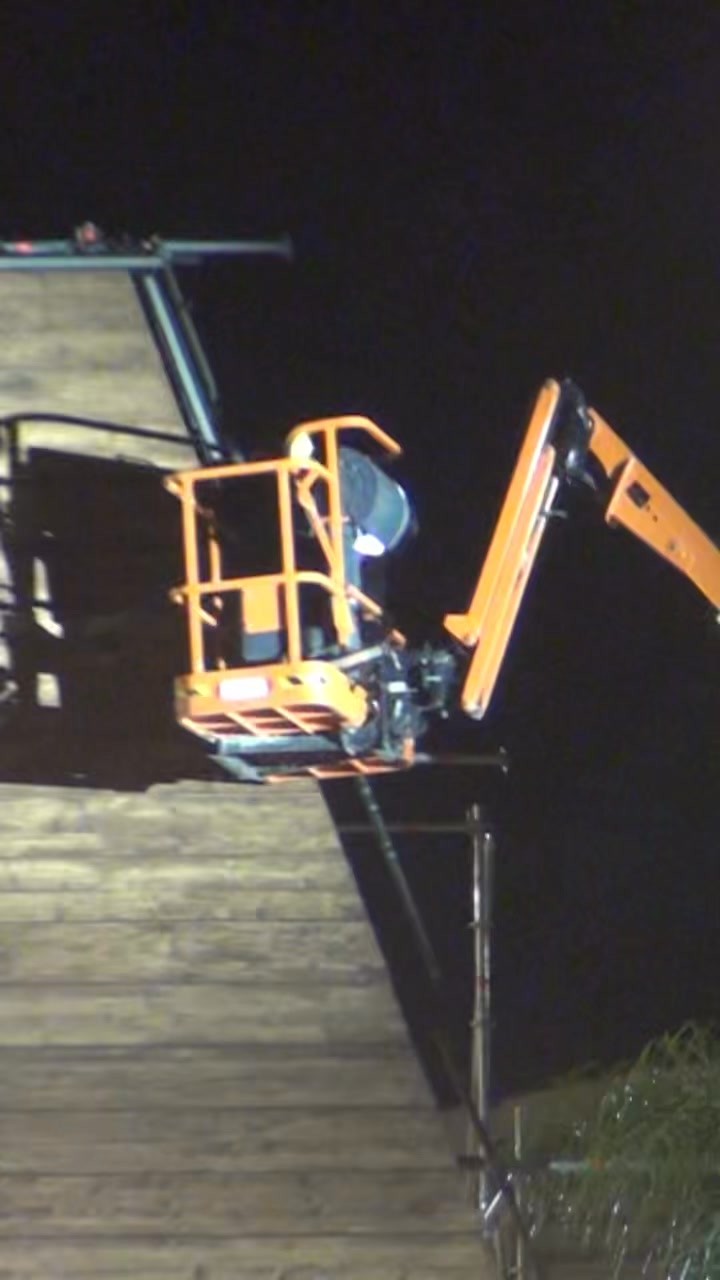 Night-time technical set-up: a cherry picker used to install a lighting fixture on a wooden stage structure.