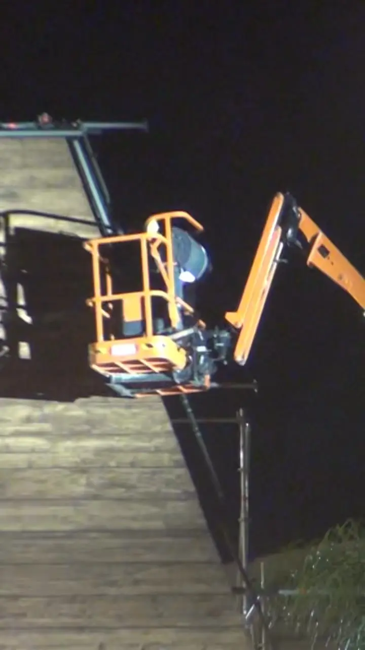 Montage technique de nuit : nacelle élévatrice pour l'installation d'un projecteur sur une structure de scène en bois.