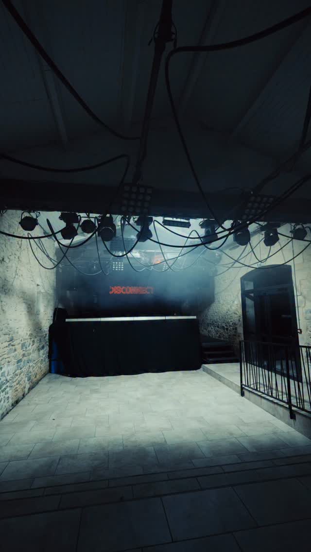 Stone-walled club interior, DJ booth beneath a truss of moving-head fixtures, red neon "DISCONNECT" sign in stage haze.